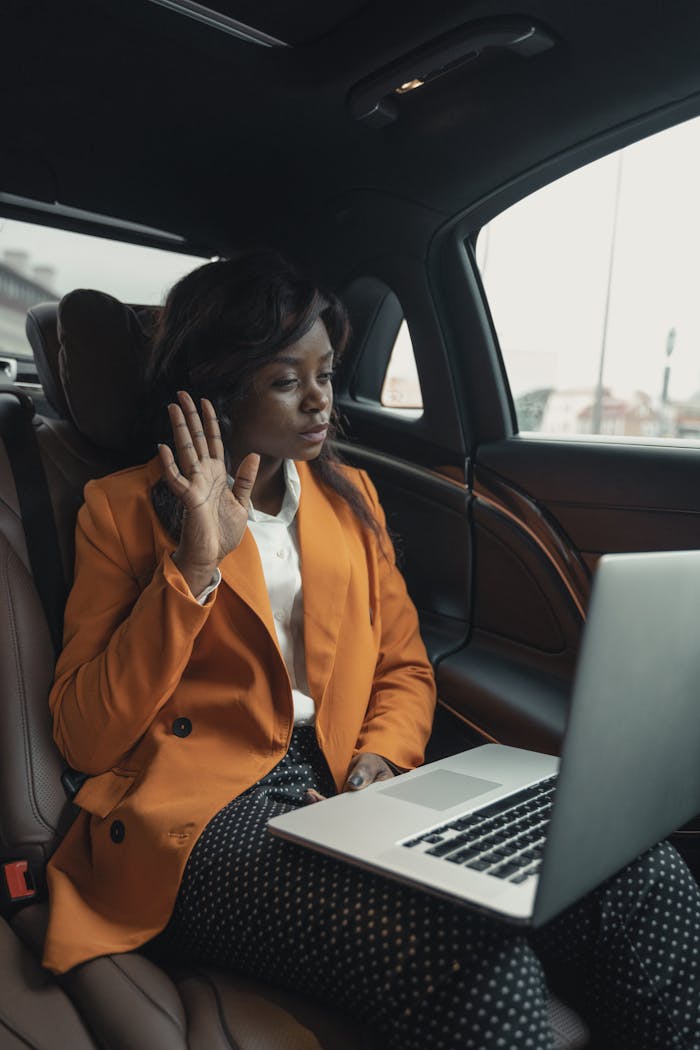 Services Confident businesswoman conducting a video call on her laptop while sitting in the back seat of a car.
